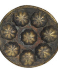 Bronze antique Indonesian cake mold with 7 flower-shaped cups and 2 side handles, close-up on plain surface.