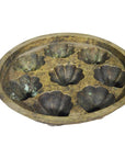 Vintage brass Indonesian cake mold with eight shell-shaped cavities, rustic patina, close-up on plain surface.