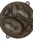 Brown metal Indonesian cake mold with crab, clam, two oval shapes, and two hanging holes, close-up view.