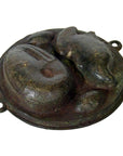 Close-up of round, weathered metal Indonesian cake mold with frog and kidney designs, two small side loops.