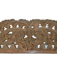 Brown wood Indonesian wall carving with intricate floral and vine cut-out designs, close-up view.
