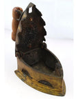 Close-up of antique Indonesian coal iron with a wooden handle and open lid, metal body, on plain background.