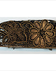 Close-up of a black rectangular antique Indonesian batik stamp block with intricate gold floral and dotted patterns.