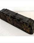 Brown wooden Indonesian batik stamp block with floral patterns and textured edges on a white surface, close-up view.