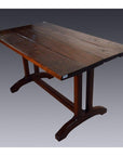 Dark teakwood plank dining table with sturdy trestle legs, placed against a gradient background.