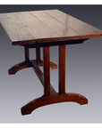 Brown wood dining table with plank top and sturdy base, set indoors against a neutral background.