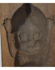 Brown wooden antique Indonesian mold with hand carved cartoon baby, large eyes, and raised arms, close-up view.