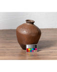 Brown ceramic Japanese oil jar with weathered, irregular shape on wooden floor, color calibration card in front.