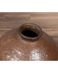 Close-up of antique Japanese brown ceramic oil jar with weathered, irregular shape and narrow opening on wood surface.