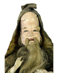 Close-up of antique Japanese Edo samurai doll in old fabric clothes, tall hat, long beard, cracked forehead, missing feet.
