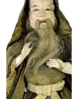 Close-up of an antique Japanese Edo Samurai doll with long gray beard, smiling face, and brown hooded robe.