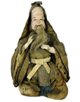 Close-up of antique bearded Japanese Edo Samurai doll in worn brown hooded robe, kneeling, missing feet.