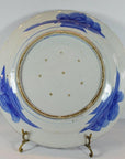 Blue and white ceramic Japanese plate with hand-painted brushstrokes and small holes, on a brass stand.