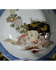 Close-up of antique Japanese porcelain bowl with hand painted old man, chest, flowers, and gold-blue detailing.