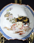 Antique Japanese porcelain dish, hand painted, white with patterns, placed beside a black and gold chest on a surface.