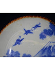 Close-up of brown-rimmed ceramic Japanese Igezara transferware plate with blue birds, clouds, and Mt. Fuji motif.