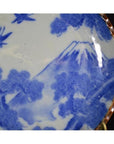 Blue and white ceramic Igezara transferware plate with mountain, trees, birds, and gold rim, close-up view.