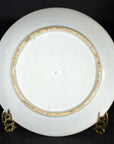 Close-up of the back of an antique Japanese Igezara transferware plate with gold rim on a metal stand.