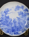 Blue and white ceramic Igezara transferware plate with floral and bird pattern on stand against a dark background.
