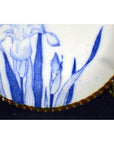 Close-up of blue floral pattern on white porcelain Igezara plate with brown textured rim, against black background.