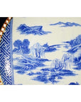 Blue and white ceramic Igezara Japanese transferware plate with trees, mountains, and patterned border, close-up view.