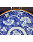 Blue and white porcelain Igezara plate with floral patterns, antique style, gold-colored hanger at top, close-up view.