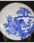 Blue and white ceramic Igezara transferware plate with floral and landscape designs on brass stand, black background.