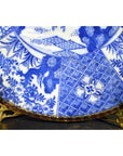 White and blue porcelain plate with floral and geometric designs on a gold stand.