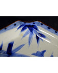 Close-up of blue and white porcelain Japanese Imari bowl with hand-painted floral designs and scalloped brown-edged rim.