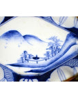 Blue and white porcelain Imari bowl with hand painted landscape of mountains, trees, and a bridge.