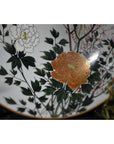 Close-up of a porcelain Kutani bowl, hand painted with white and orange flowers and green leaves, antique style.