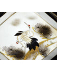 White porcelain Kutani dish with two white cranes, red crowns, and pine branches on a white background.