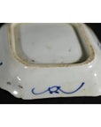 Close-up of antique Japanese Kutani porcelain dish with blue hand-painted scrolls on an aged white ceramic base.