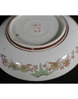 White porcelain plate with pink flowers and green leaves, shown upside down.