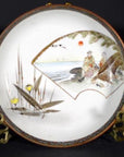 Close-up of multicolor Kutani porcelain plate with two figures, birds, reeds, and red sun on dark background.