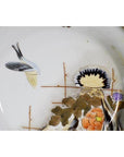 White porcelain Kutani plate with hand-painted bird, flowers, and gold-accented branches, close-up.
