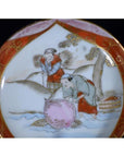Close-up of an antique Japanese Satsuma porcelain plate with two figures by a river under a tree, one holding a basket.