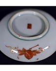 Red and gold porcelain plate underside with hand-painted floral patterns and a red mark, close-up.