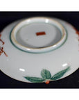 White porcelain plate with green leaf design and red mark, antique Japanese Satsuma, close-up on plain background.