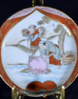 Close-up of vibrant red and gold hand-painted ceramic Japanese Satsuma plate with two figures by a river.