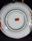 Close-up of underside of antique Japanese Satsuma porcelain plate with red floral designs and small red center mark.