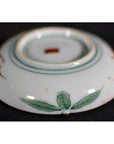 Close-up of the base of an antique Japanese Satsuma plate with green leaf designs and a red central mark.