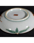 Close-up of the underside of a ceramic Satsuma plate with green leaf motif and small red square mark at the center.