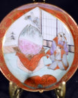 Close-up of antique Japanese Satsuma porcelain plate with red border, figures in traditional dress opening a giant peach.