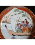 Close-up of an antique Japanese Satsuma ceramic plate with red border, painted sailboat figures, and scenic landscape.