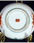 Close-up of bottom of antique Japanese Satsuma porcelain plate with red floral designs and red square mark on stand.