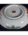 Close-up of an antique Japanese Satsuma porcelain plate with green leaf designs and a red mark on the base.