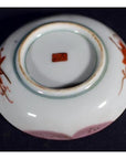 Close-up of an antique Japanese Satsuma porcelain plate with red floral designs and a red stamp.