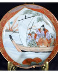 Close-up of a multicolor ceramic Satsuma plate with two figures on a sailboat, trees, and waves hand painted.