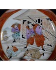 Colorful ceramic Satsuma plate with samurai in robes and spears battling near a building, two figures lying nearby.